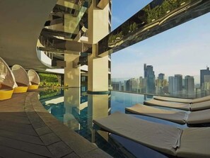 Et roolftop-infinity pool med liggestole, gelænder af glas og udsigt over byens skyline.