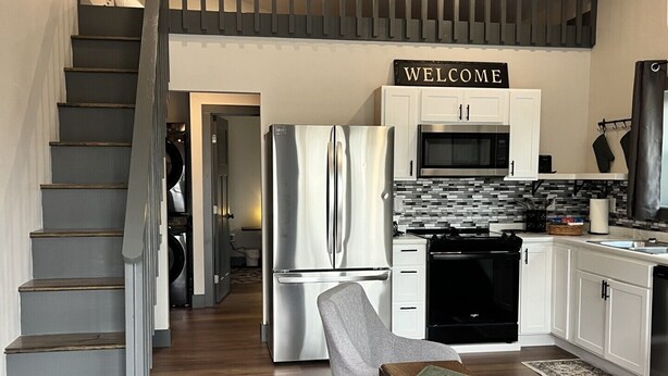 Een moderne keuken met een roestvrijstalen koelkast, een magnetron en een zwarte oven. Boven de kastjes hangt een bord met de tekst 'WELCOME'.