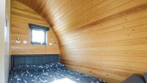Una habitación tipo cabaña con techo inclinado, una cama con colcha estampada, una ventana y una pequeña mesa.