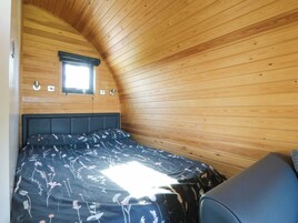 Una habitación tipo cabaña con techo inclinado, una cama con colcha estampada, una ventana y una pequeña mesa.
