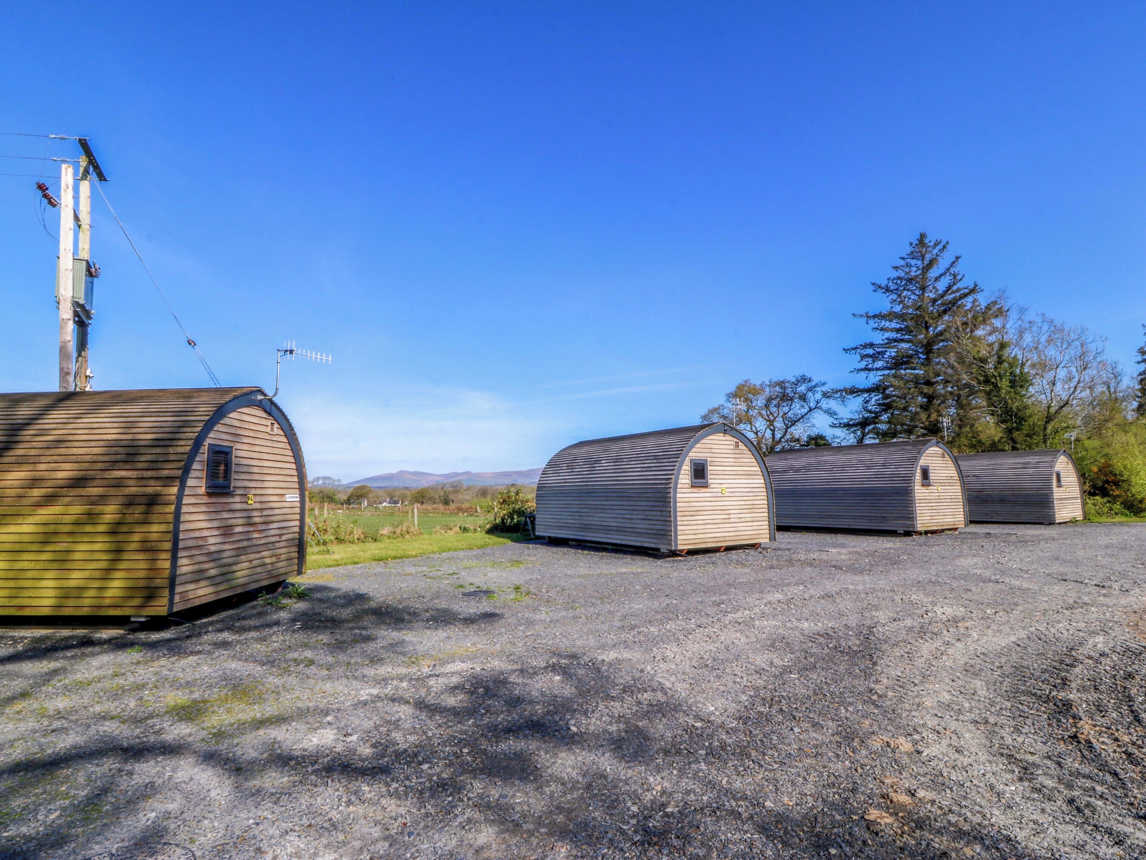 Three wooden cabins with arched roofs, a gravel ground, and a clear blue sky.