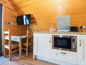 Uma cozinha compacta com paredes de madeira, micro-ondas, torradeira e televisão fixada acima do balcão.