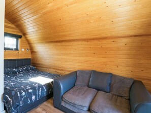 Quarto aconchegante com teto inclinado, cama com roupa de cama florida, sofá com almofadas e uma janela.