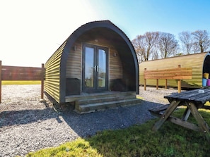 A small, single-story wooden structure with a curved roof, a front door, and a small porch. - Bron Eifion Pod 5 (Criccieth)