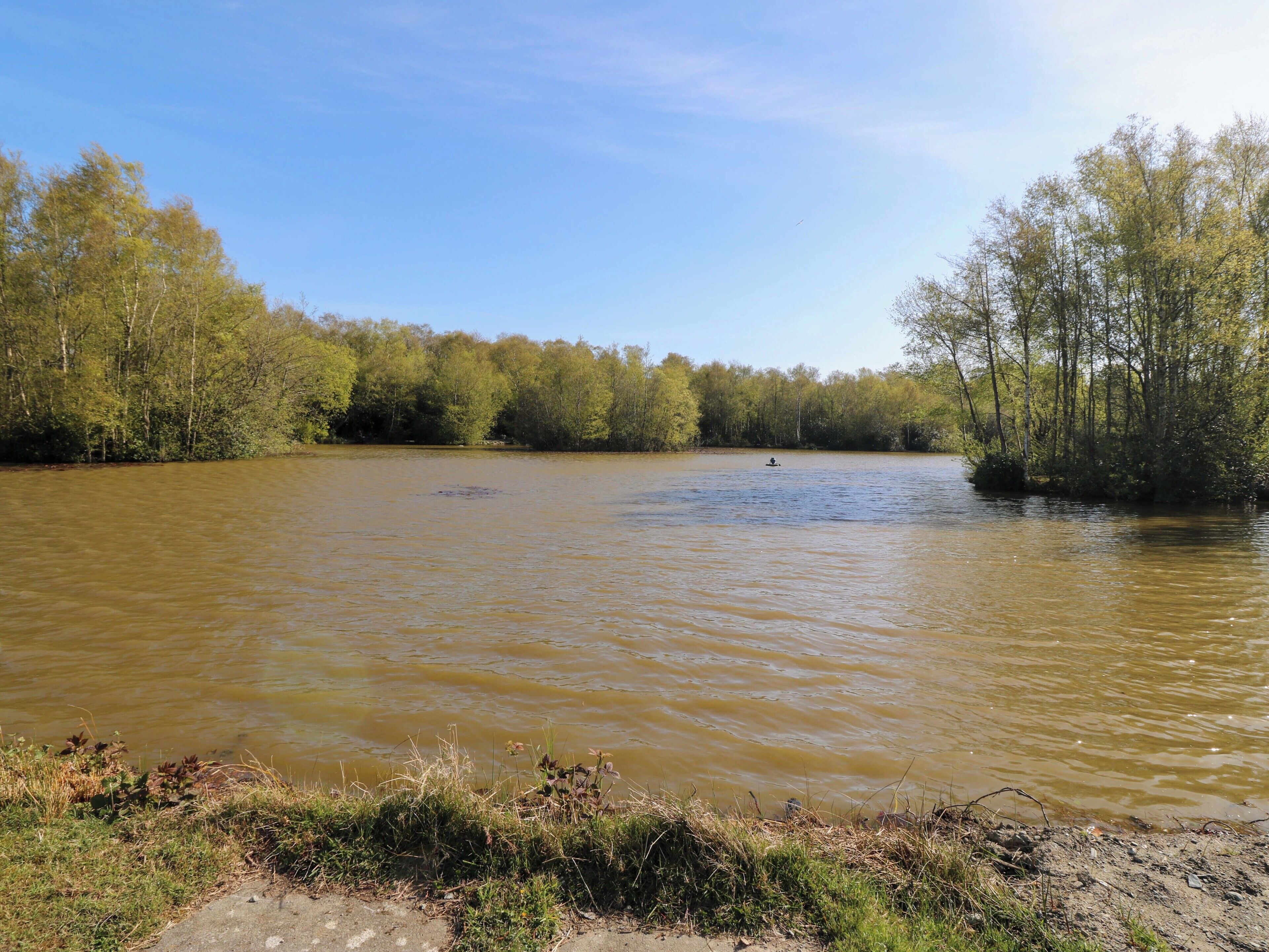 Een rivier met bomen aan weerszijden, een heldere lucht en iemand die peddelt.