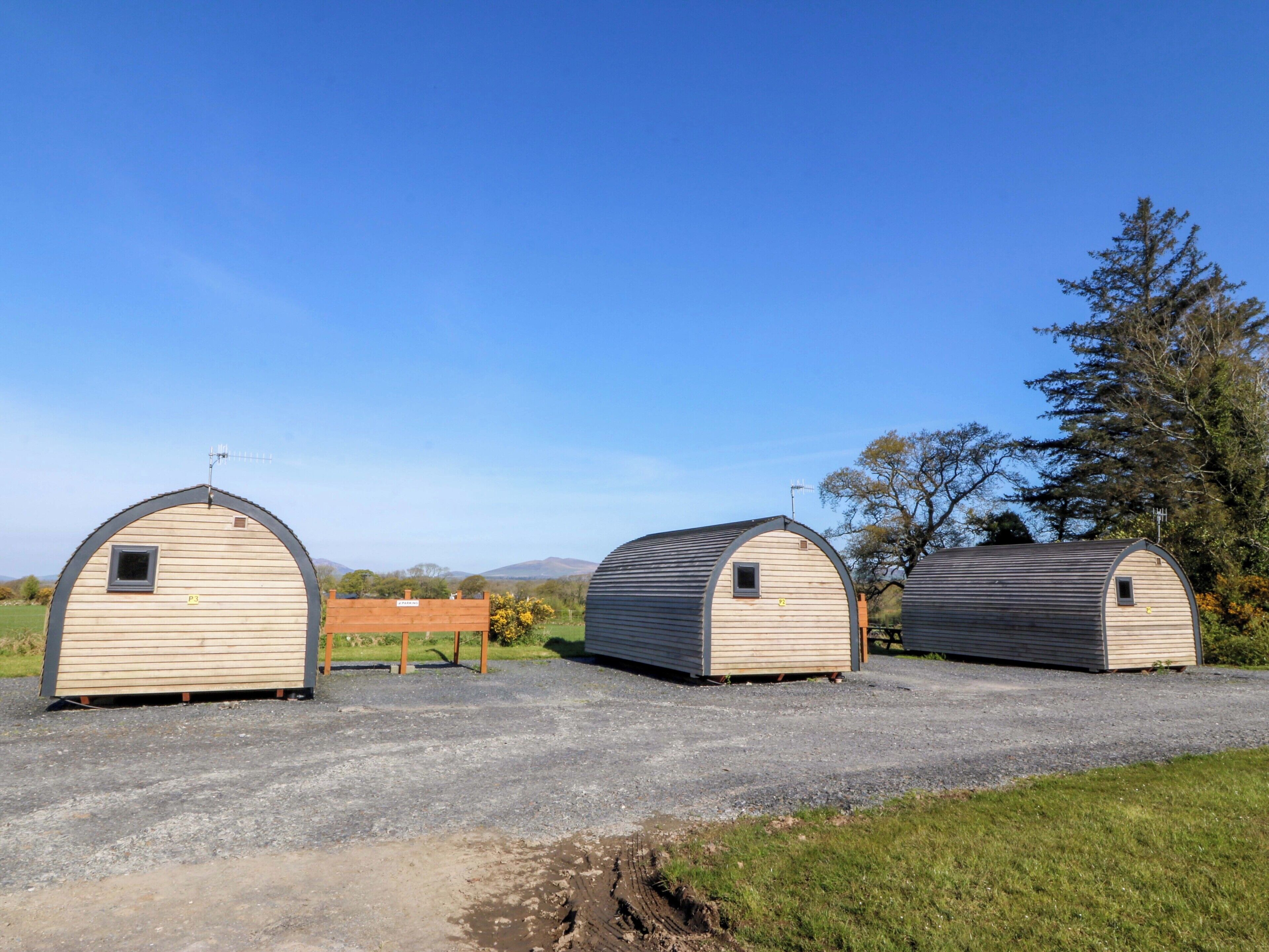 Three small, arched, wooden structures with metal roofs, labeled P3, P4, and P5, on a gravel path with grass on the sides, under a clear blue sky.