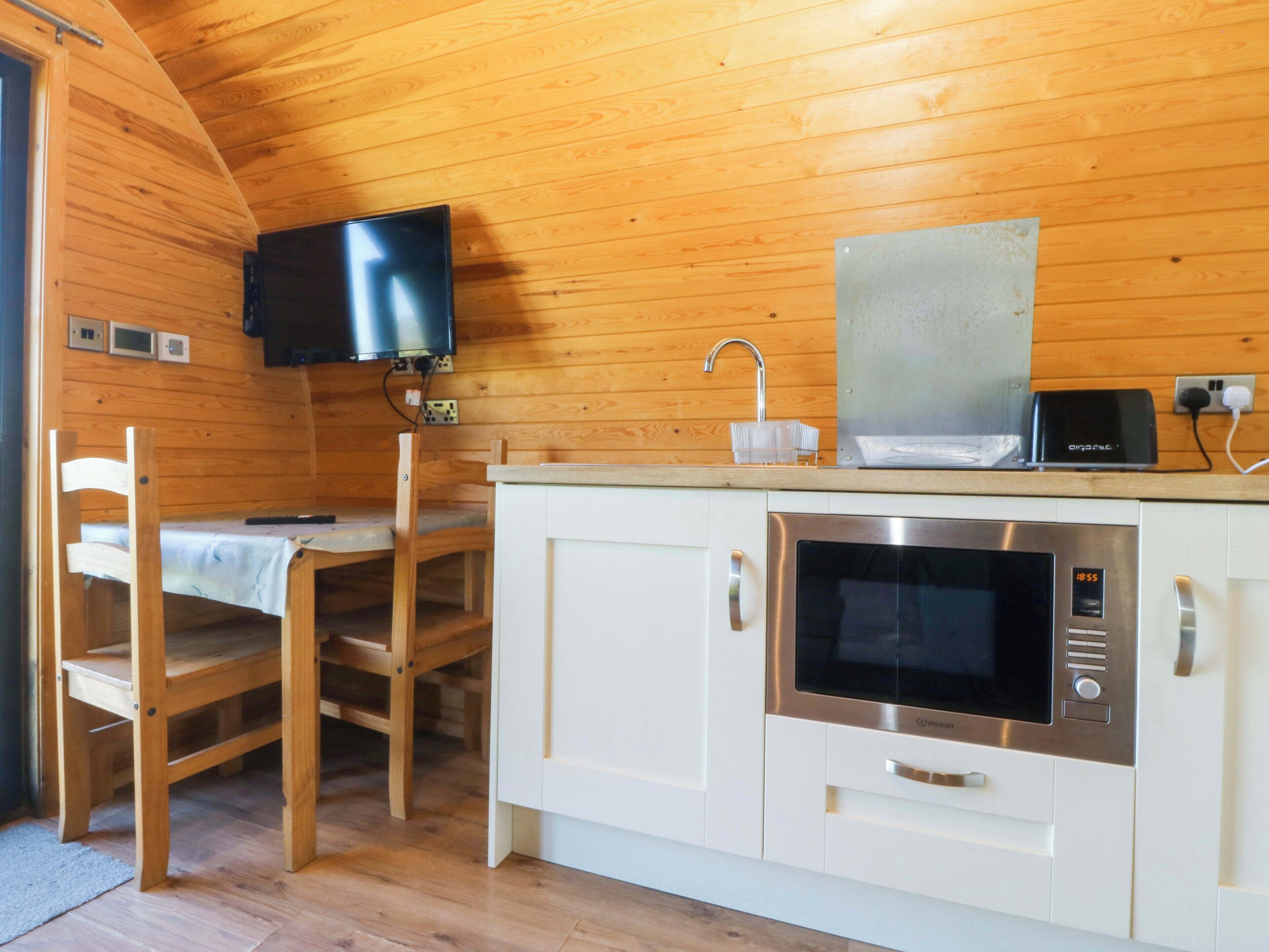 Cocina compacta con microondas, tostadora y televisor montado en la pared.