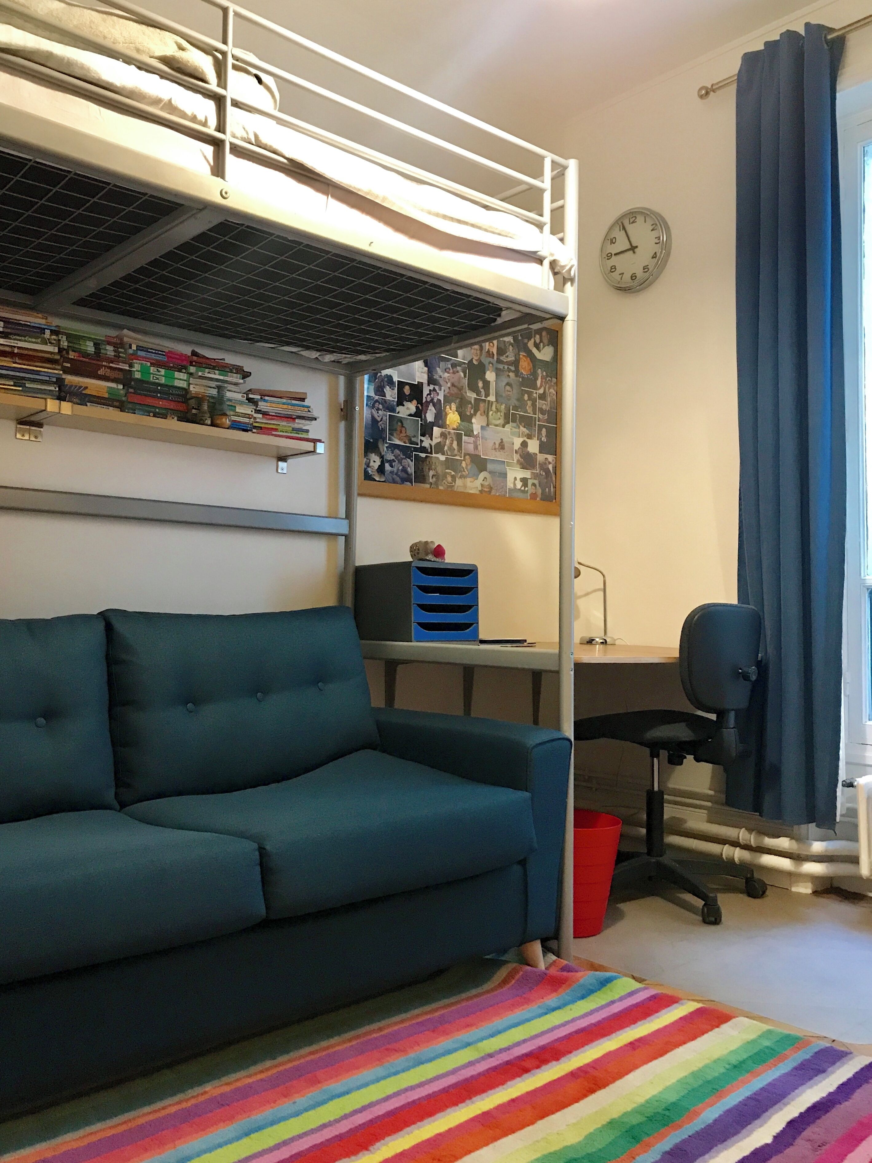 Una cama litera con escritorio y silla, un sofá, una alfombra colorida y una pared con fotos.