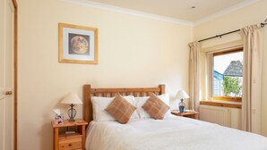 Een slaapkamer met een houten bed, twee nachtkastjes met lampen, een lijst met een afbeelding aan de muur, en een raam met gordijnen.
