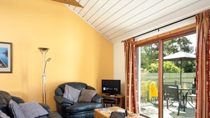 Een woonkamer met een bank, een salontafel, een televisie en een schuifdeur die leidt naar een buitengebied met een tafel en stoelen.