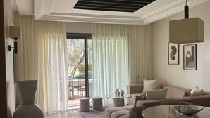 A modern living room with a sofa, a round table, and a large window with sheer curtains. - Comfortable apartment at Vizir Center Parc (Marrakech)