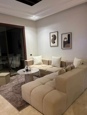 A living room with a beige sectional sofa, a small round coffee table, and two framed artworks on the wall. - Comfortable apartment at Vizir Center Parc (Marrakech)