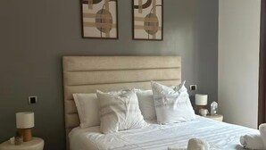 A neatly made bed with white linens, two bedside tables with lamps, and abstract wall art. - Comfortable apartment at Vizir Center Parc (Marrakech)