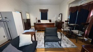 Ein Zimmer mit einem Bett, einem Schreibtisch, einem Stuhl, einer Couch und einem Esstisch.