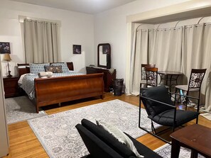 A bedroom with a wooden bed, a small table, a chair, a mirror, and a window with curtains. - 1 FREE parking spot - Coolidge Corner-Close to T (Brookline)