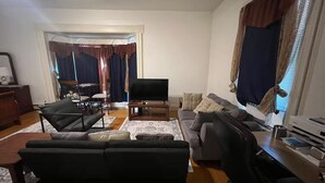 Ein Wohnzimmer mit Sofa, Fernseher, Couchtisch und einem Essbereich mit Stühlen und Tisch.