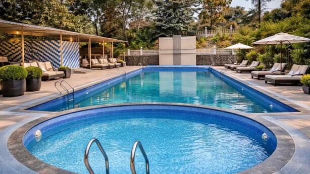 A rectangular swimming pool with a hot tub in the center, surrounded by lounge chairs and umbrellas.