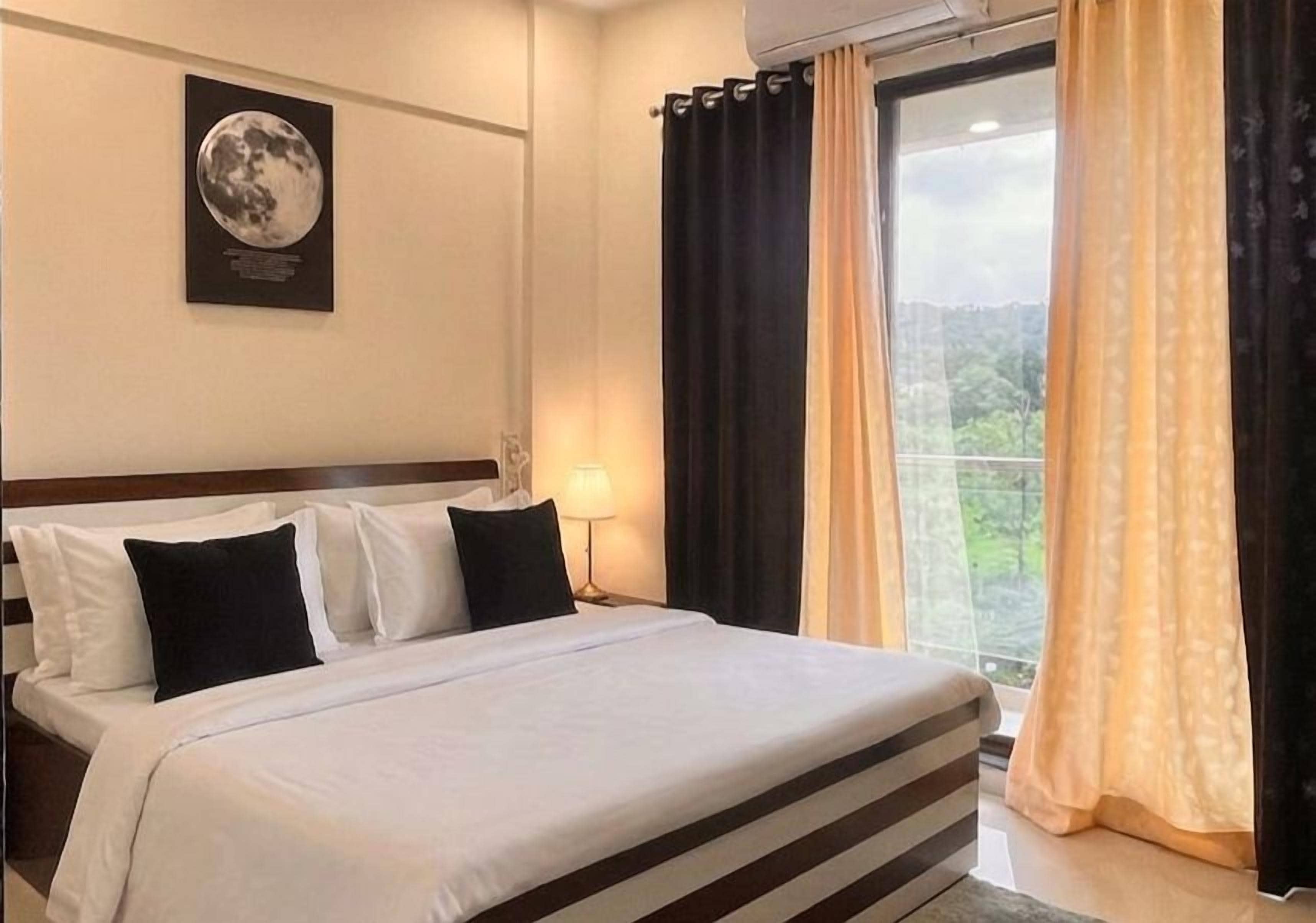 A hotel room with a bed, a nightstand, a lamp, and a window with curtains.