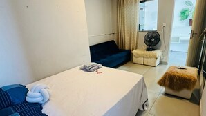 Una habitaci ón con una cama, un sofá azul, una mesita con un ventilador y vistas al exterior.