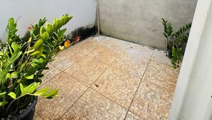 Un piccolo patio recintato con pavimento in piastrelle, parete in cemento e piante in vaso.