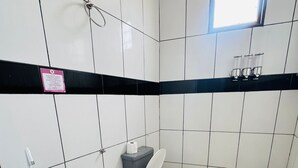 Un baño con paredes de azulejos blancos, una franja decorativa negra, un lavamanos, un inodoro y un cubo de basura.