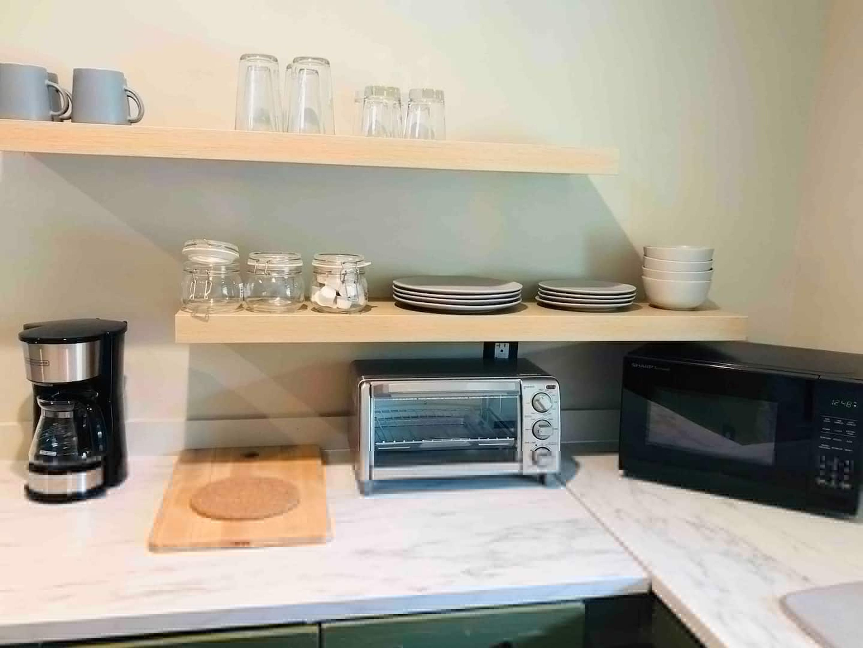 Una cocina con cafetera, tostadora, microondas y estantes con frascos y platos.