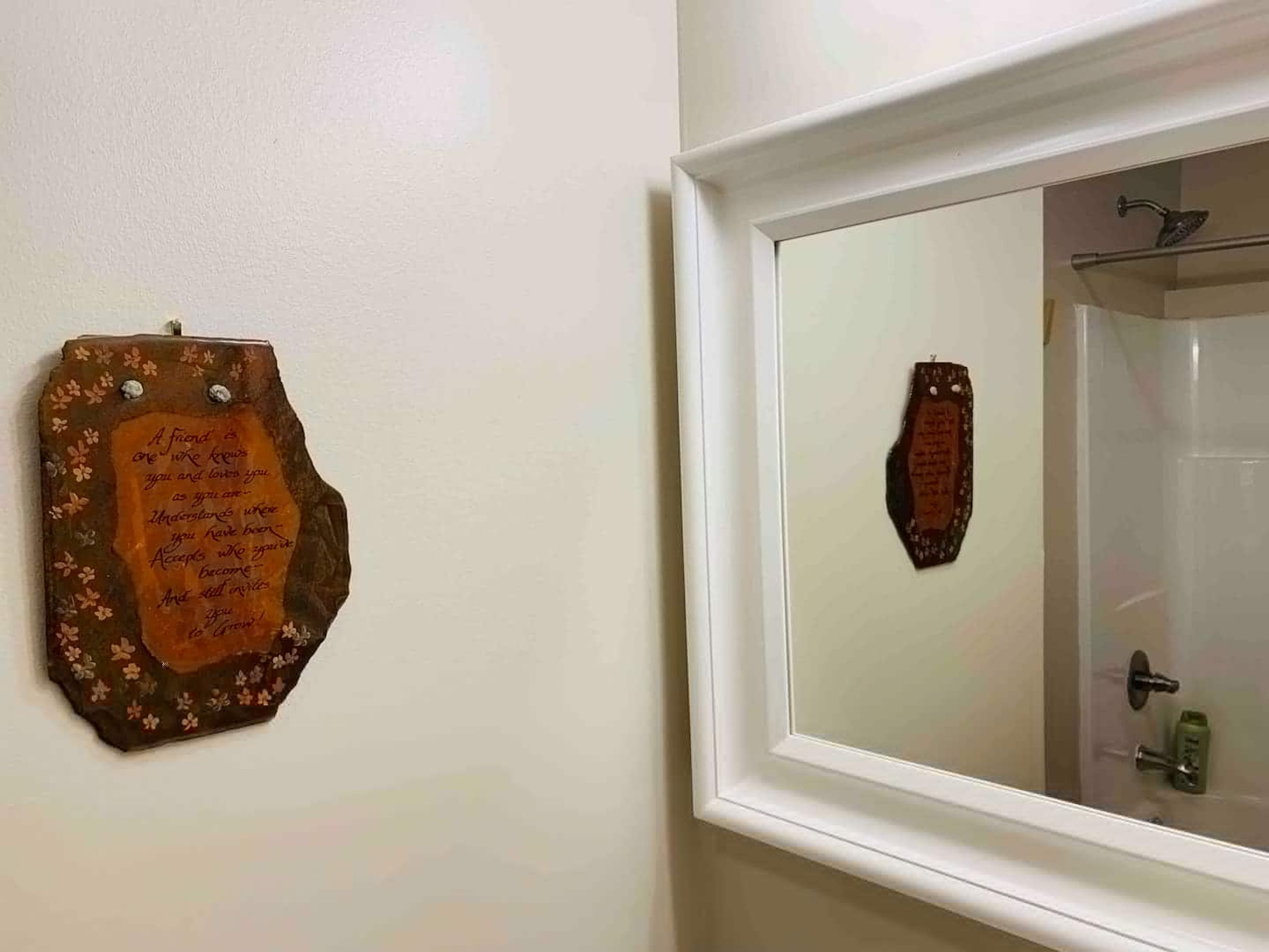 A bathroom with a mirror, a shower, and a wall-mounted plaque.
