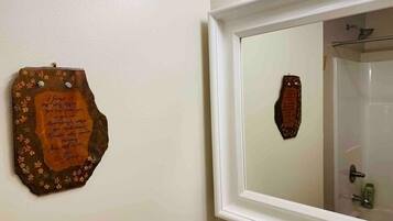 A bathroom with a mirror, a shower, and a wall-mounted plaque.