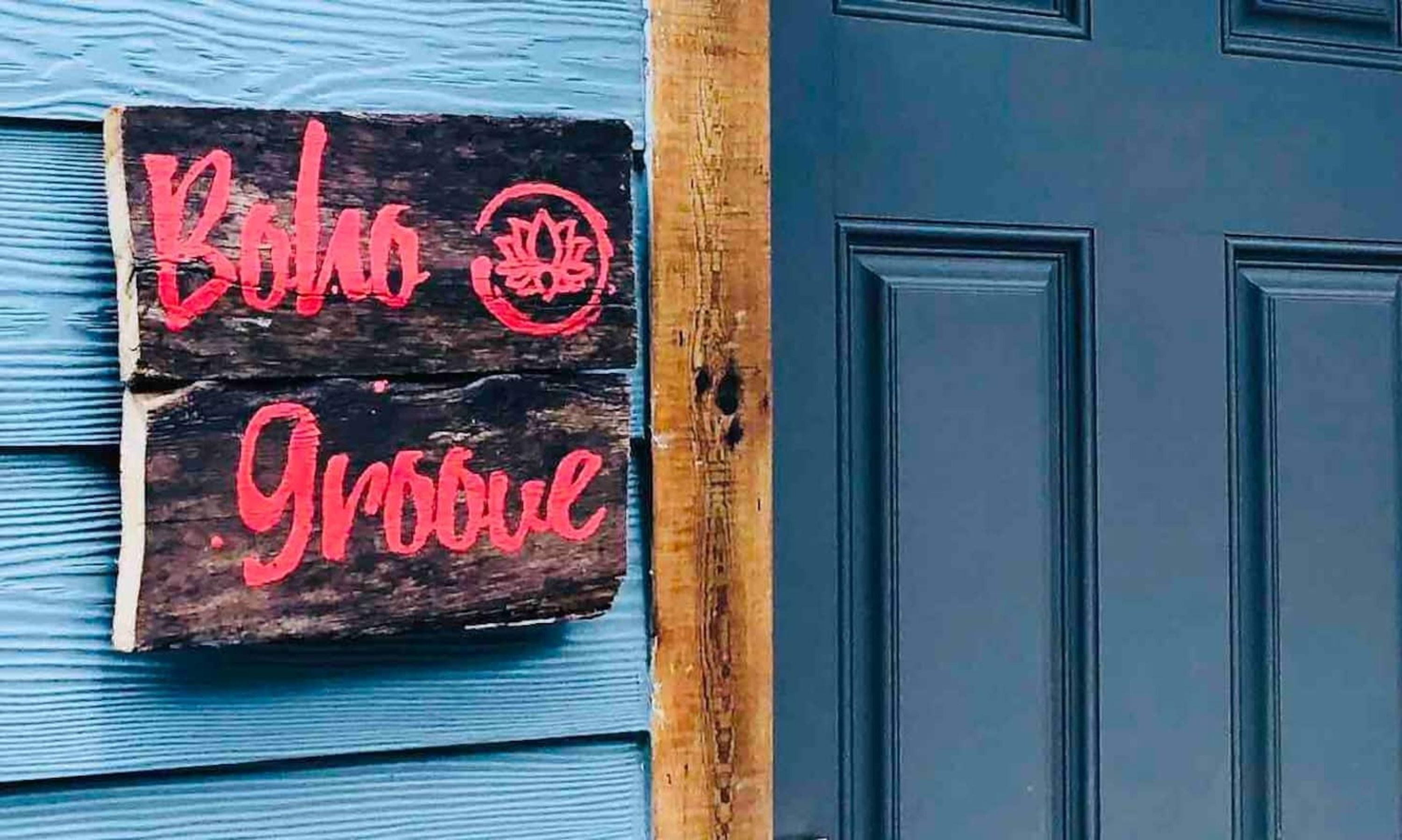 Une enseigne en bois avec du texte rouge sur une porte bleue.