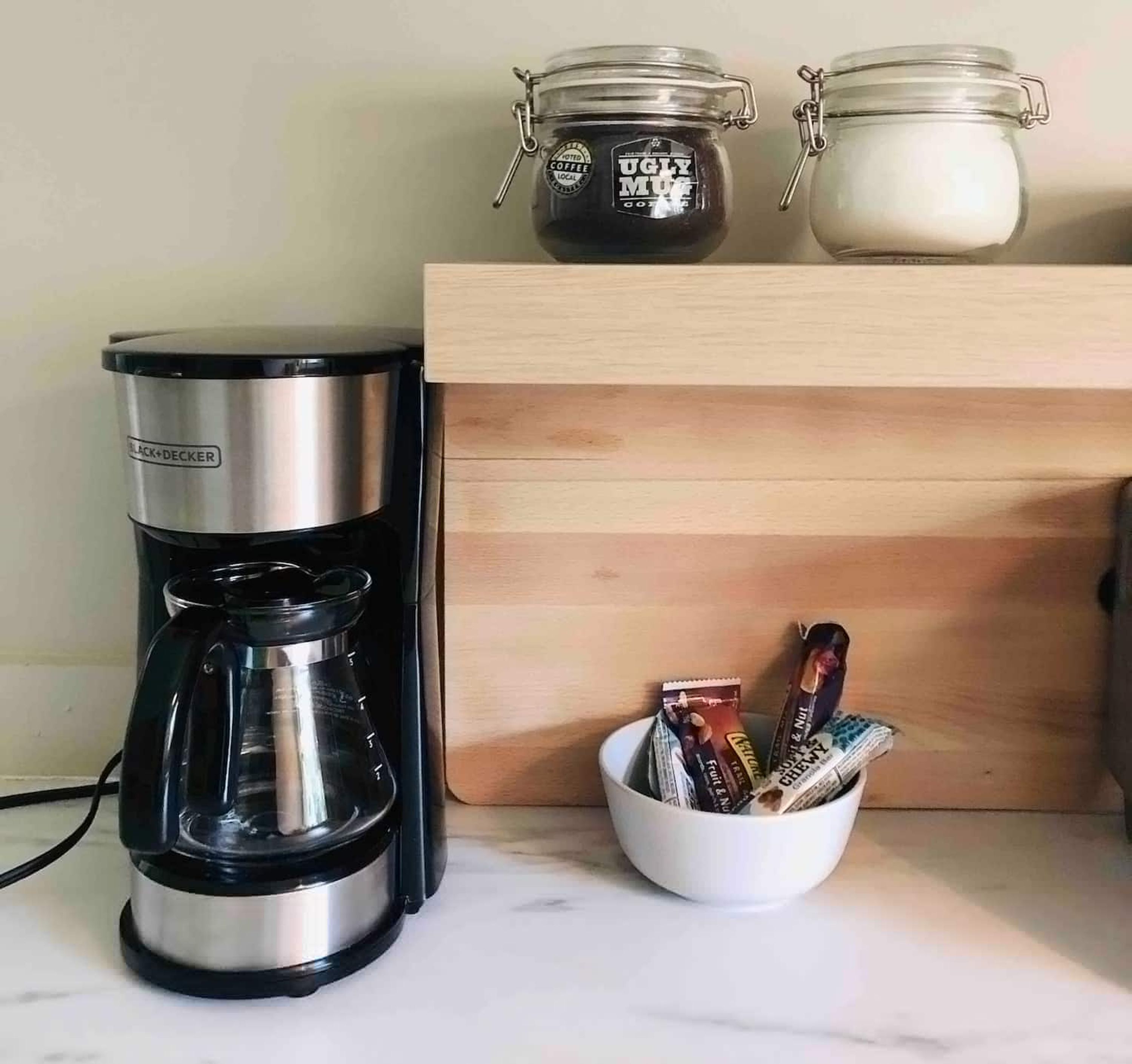 Eine Kaffeemaschine, zwei Gläser und eine Schüssel mit Snacks auf einer Küchenarbeitsplatte.