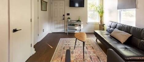 A living room with a sofa, a television, a door, and a window with a plant.