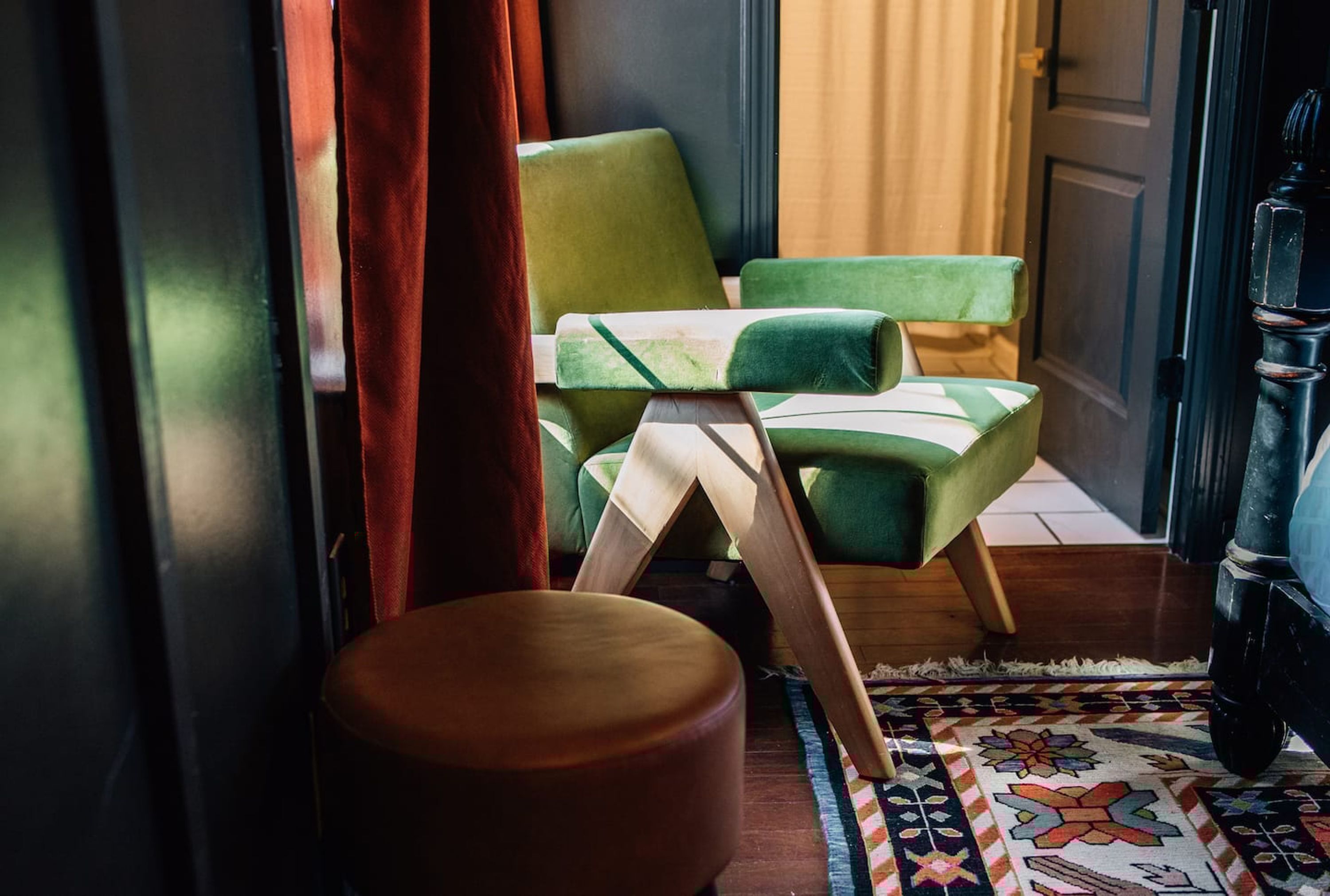 A room with a green armchair, a wooden stool, and a patterned rug.