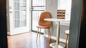 A room with a wooden floor, a brown chair, a small round table, and a window with blinds. - Moody Blues Studio Perfect for Work or Romance (Memphis)
