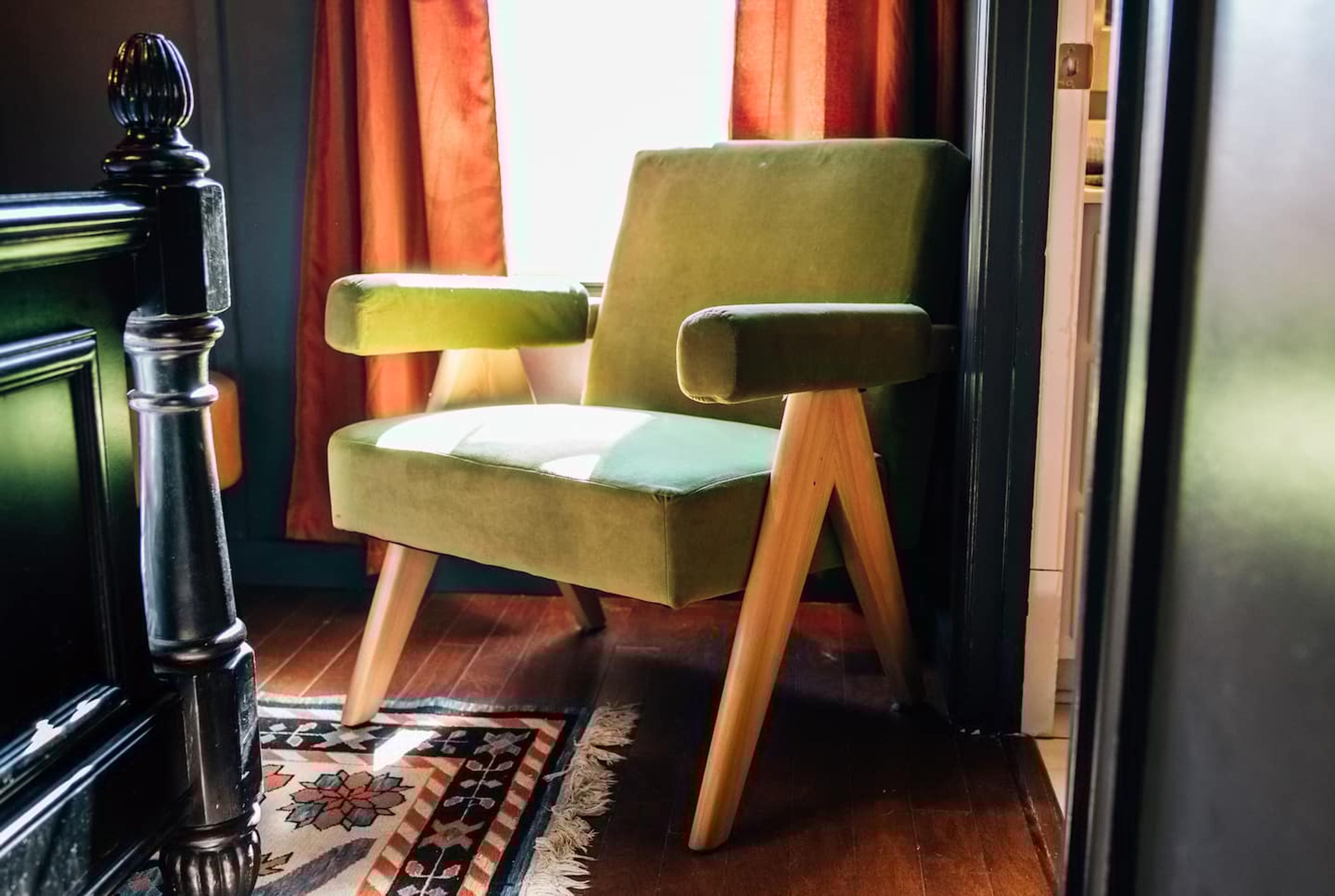 Uma poltrona verde com pés de madeira, um tapete estampado e um armário de madeira escura.