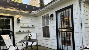 A corner of a house with a black door, white siding, a small table with chairs, and string lights. - Moody Blues Studio Perfect for Work or Romance (Memphis)