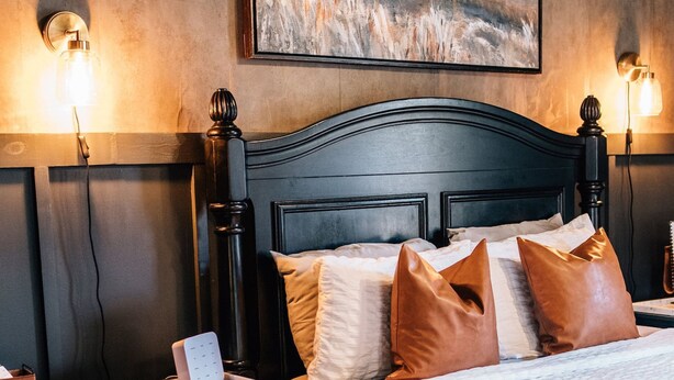 A bedroom with a dark wood headboard, a patterned rug, and a painting on the wall. - Moody Blues Studio Perfect for Work or Romance (Memphis)