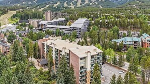 Ein beliebtes Feriengebiet mit mehreren Gebäuden, darunter ein großes, modern gestaltetes Hotel, umgeben von dichten Wäldern und Bergen im Hintergrund.