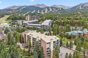 A resort area with multiple buildings, including a large hotel with a modern design, surrounded by dense forests and mountains in the background. - Breck Base Condo with Pool + Hot Tub (Breckenridge)