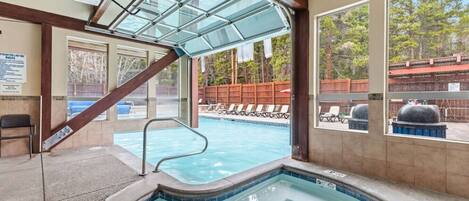 A pool area with a hot tub, a covered seating area, and a view of the surrounding landscape.