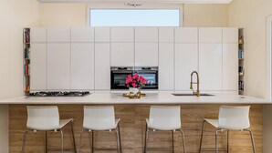 A modern kitchen with a central island, bar stools, a built-in oven, and a window above the sink. - Villa Jannah -Luxury Halal Retreat (Quinta do Anjo)