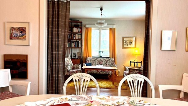 A dining area with a table set for two, a red book on the table, and a view into the adjacent living room. - 7 Person Holiday Home in Virserum (Virserum)