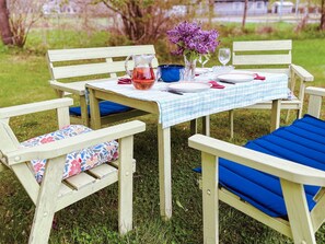 Una mesa de madera al aire libre con mantel a cuadros, una jarrón, un florero y un vaso.