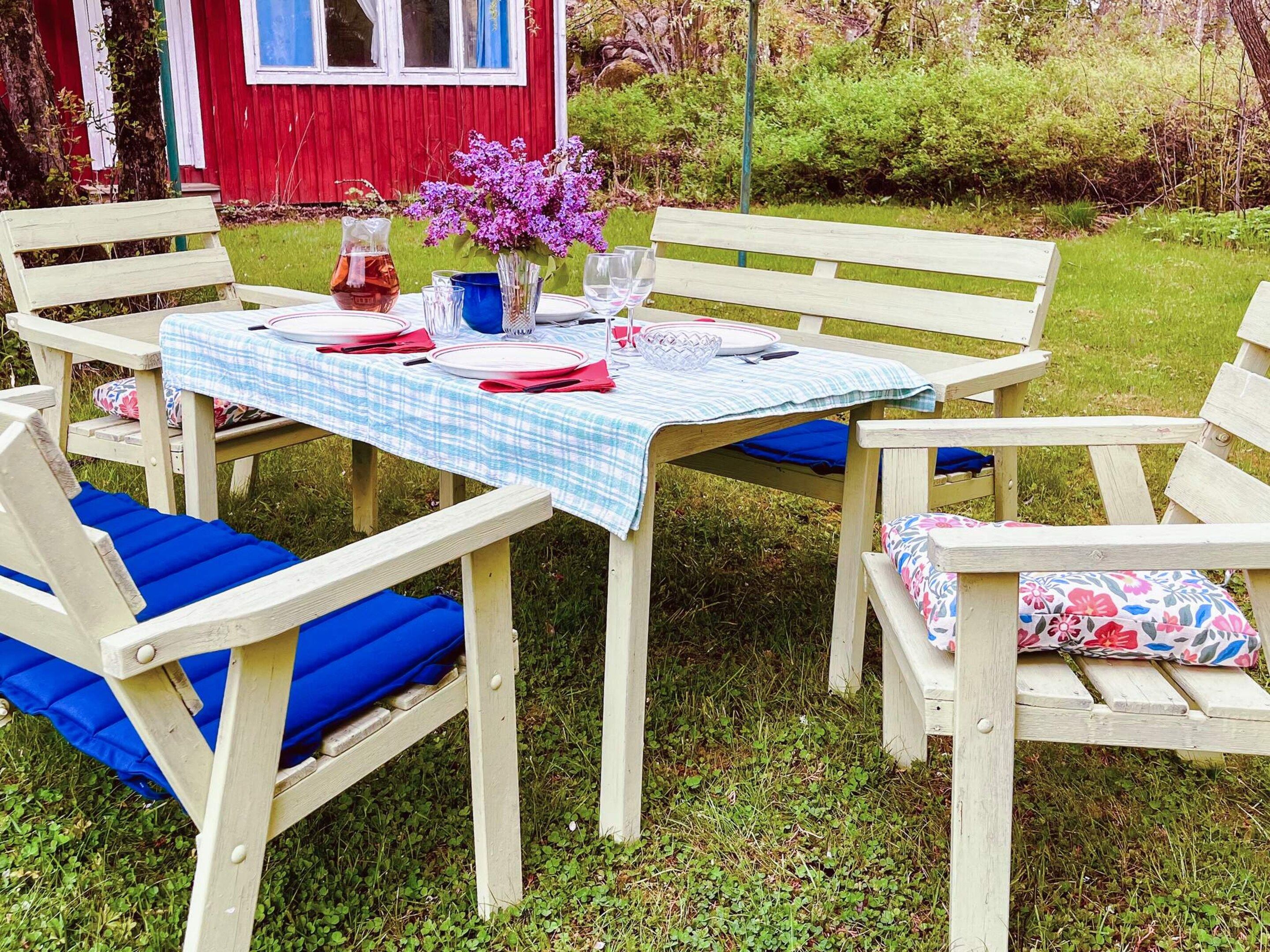 Un área de comedor al aire libre con una mesa lista para cuatro personas, rodeada de sillas de madera con cojines azules.