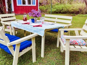 Un área de comedor al aire libre con una mesa lista para cuatro personas, rodeada de sillas de madera con cojines azules.