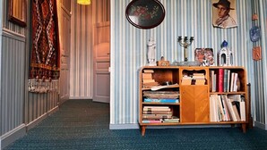 A hallway with a carpeted floor, a hanging light fixture, a bookshelf with books, a framed picture, and a decorative tapestry. - 7 Person Holiday Home in Virserum (Virserum)