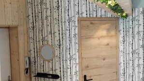 Een kamer met een houten deur, een kleine ronde spiegel, een telefoon en een zwarte kapstok aan de muur.