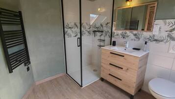 Un baño moderno con cabina de ducha de vidrio, tocador de madera y inodoro blanco.