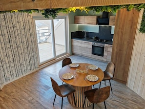 Eine moderne Küche mit Holzschränken, einem Gasherd und einer Essecke mit rundem Tisch und Stühlen.