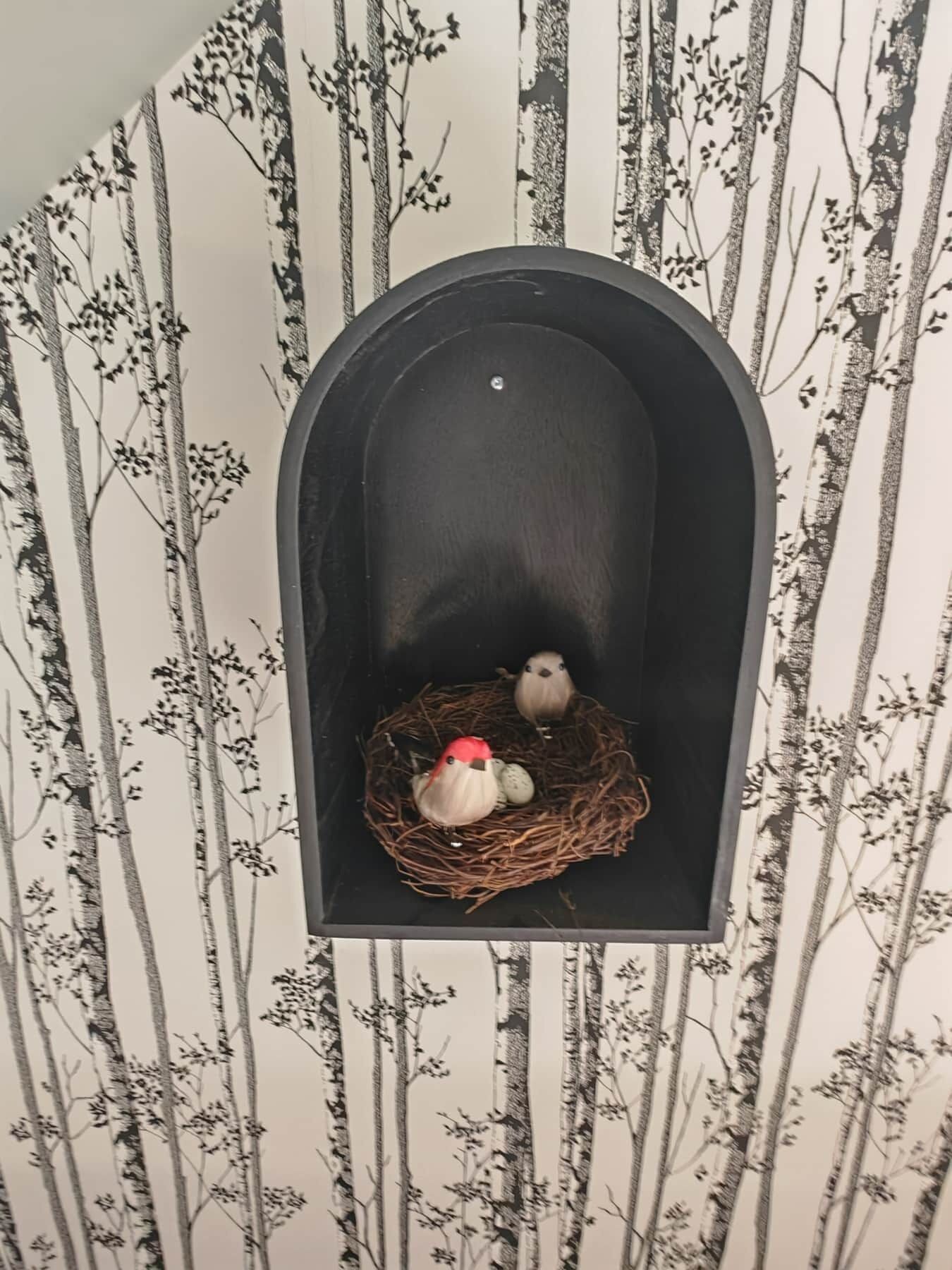 Un buzón con un nido que contiene dos pájaros decorativos y huevos.