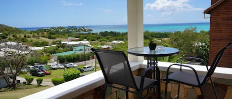 A balcony with a table and chairs, overlooking a coastal view with houses and parked cars.